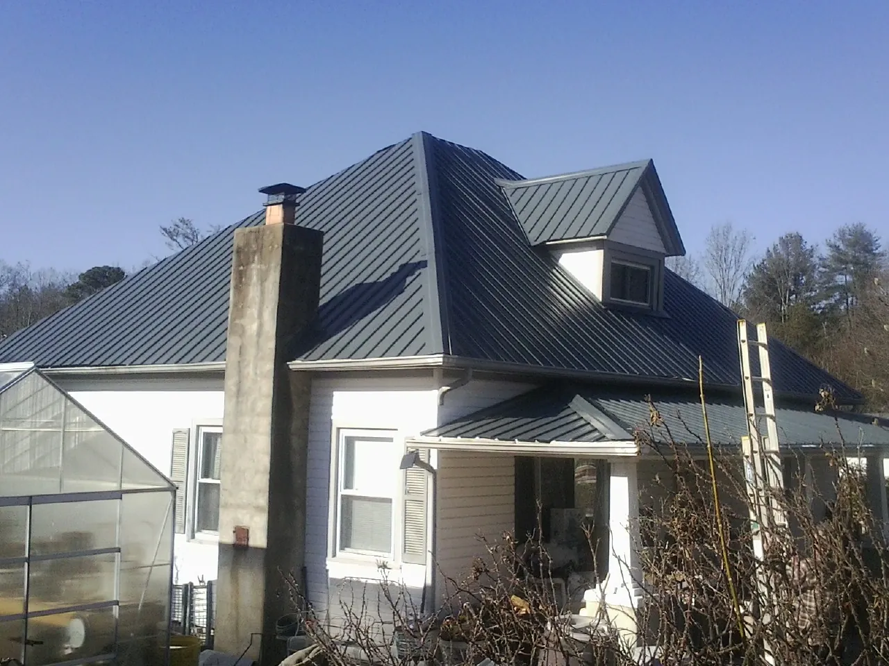 Dark blue standing seam metal roof on a white farmhouse with dormer — Slate & Tile Roof Repair by Roofing Brothers in Cummaquid