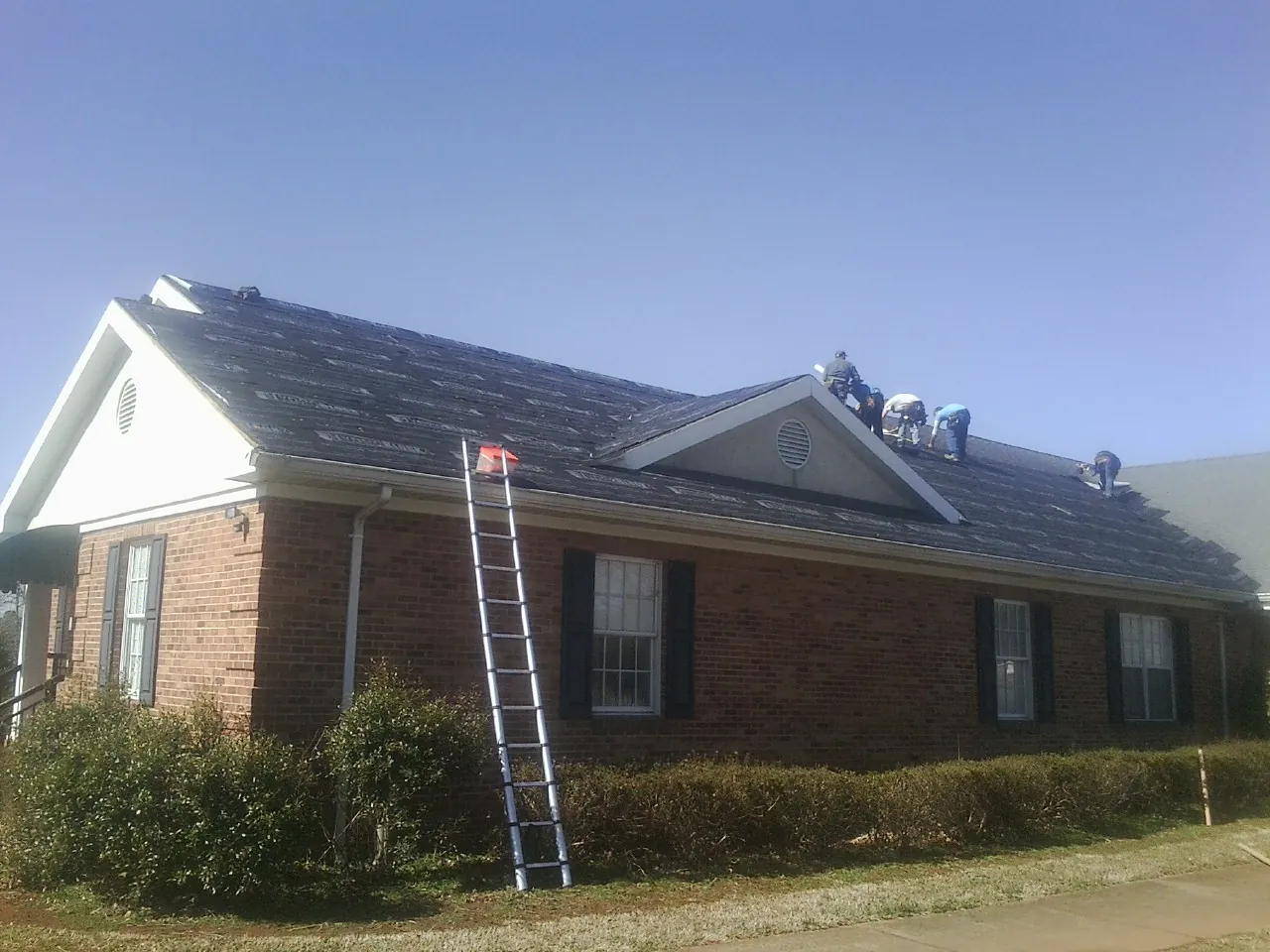 Crew tearing shingles off a brick ranch roof with a ladder set — Metal Roof Repair work by our crew in Cummaquid