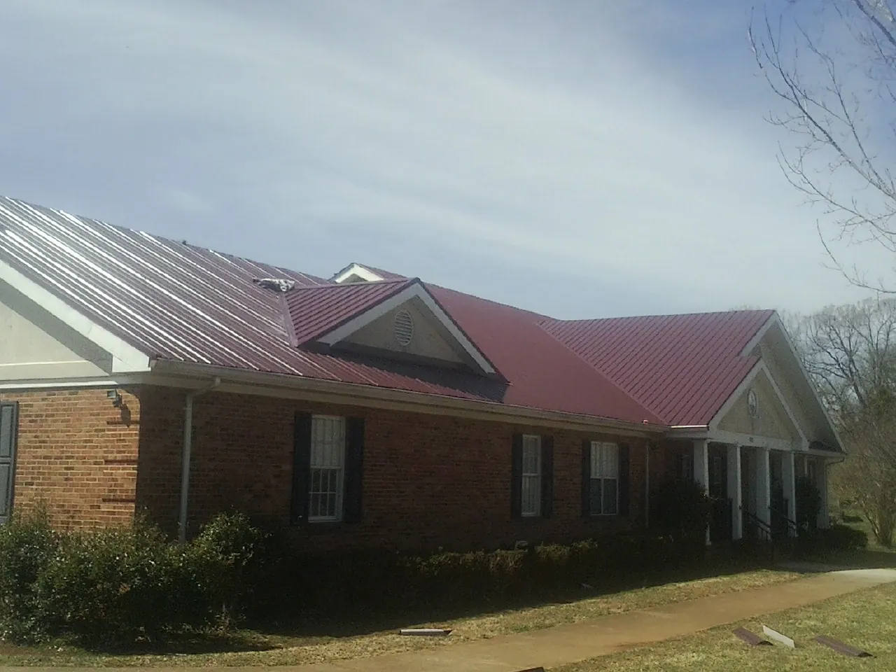 Red metal roof with gabled entries on a long brick building, from a Hail Damage Roof Repair job in Cummaquid