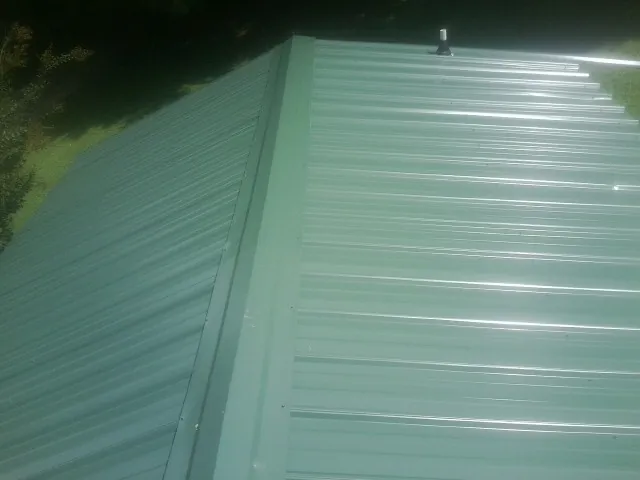 New green metal panels meeting at the ridge of a roof — Flat Roof Repair work by our crew in Cummaquid