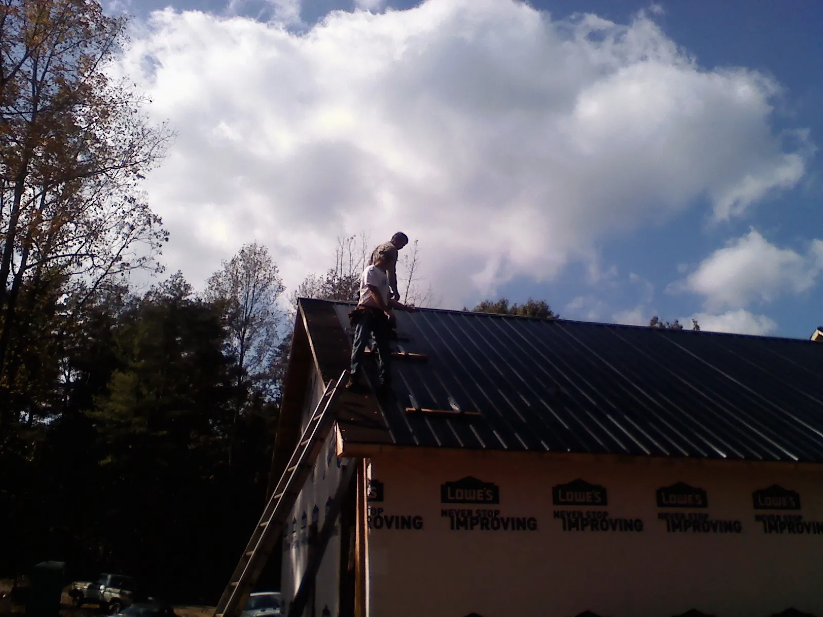 Roofer fastening dark metal panels high against a cloudy sky, from a Roof Inspection job in Cummaquid