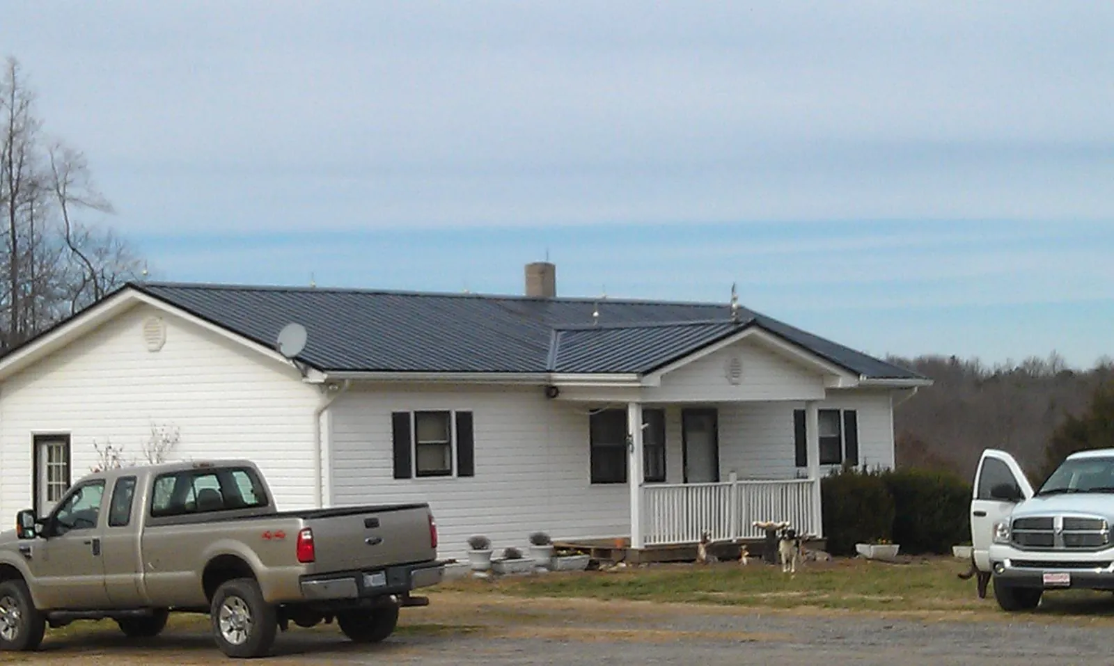 Finished dark metal roof on a white ranch home with work trucks parked in Cummaquid
