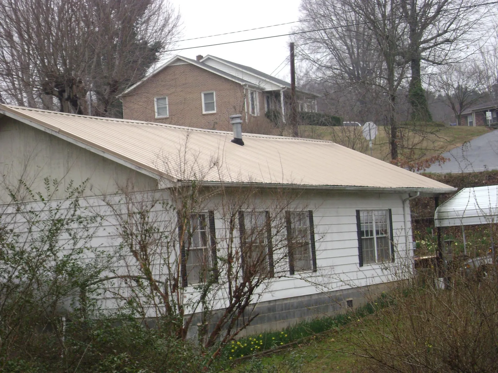 Tan metal roof on a white sided house set into a hillside — Commercial Roofing by Roofing Brothers in Cummaquid