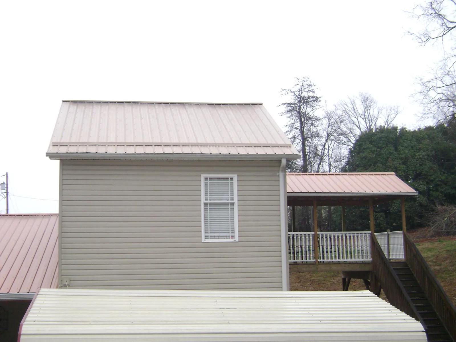 Tan metal roofs on a two story addition and attached porch, from a Roof Replacement job in Cummaquid